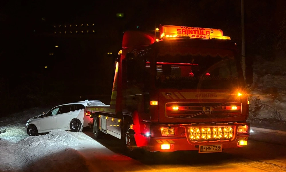 Hinaus Saintula hinausauto vetää valkoista farmariautoa ojasta pimeällä talvisella tiellä